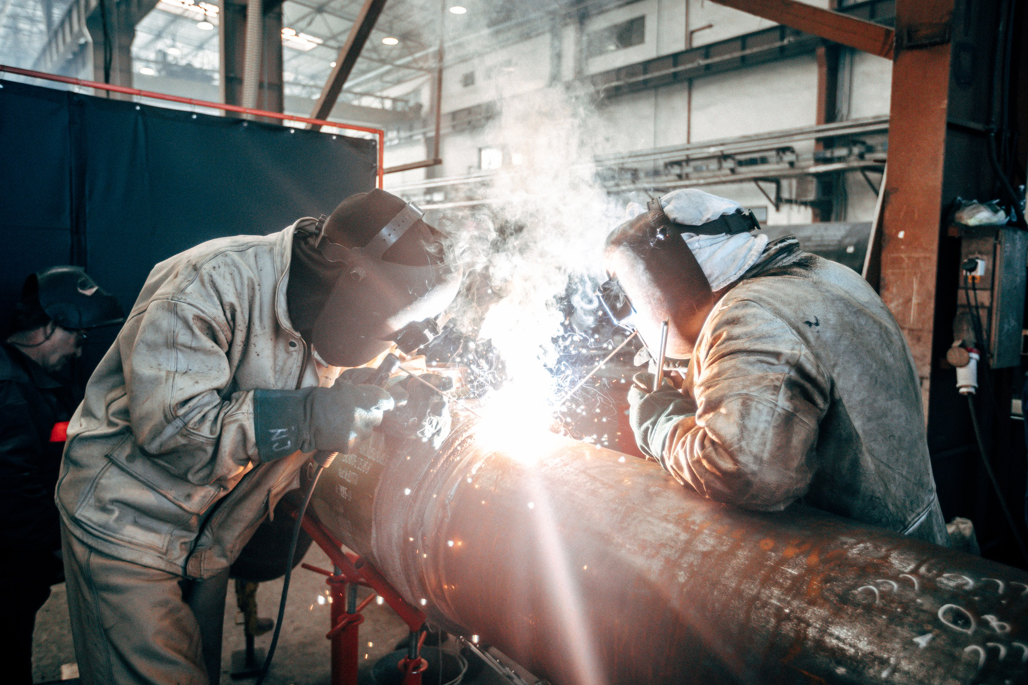 Welders with protective equipment welding pipe in the factory